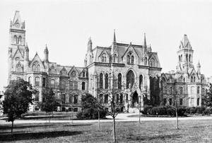 歷史悠久的哥德式大學建築，擁有石塔和拱形窗戶，周圍環繞著樹木和草地。