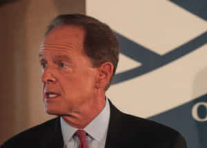 身穿西裝、打紅色領帶的男子在正式活動中發言。 — 政治 壁紙