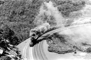 蒸汽火車蜿蜒穿過森林覆蓋的山脈，煙霧滾滾。 — 黑白 壁紙