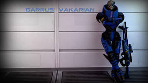 圖瑞安士兵 Garrus Vakarian 身穿藍色盔甲靠著牆壁，顯示他的名字。
