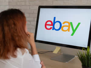 穿白襯衫的人在桌前思考，顯示器上有eBay標誌。