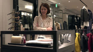 女性在服裝店展示櫃後微笑，櫃內有毛衣和手提包。