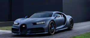 啞藍色Bugatti Chiron停泊喺瀝青路上，靠近深色牆壁同草叢。 — 3440x1440 壁紙