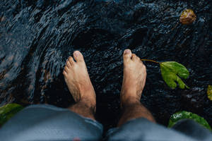 黑暗流動水中的赤腳與漂浮的樹葉 — 暗色 壁紙