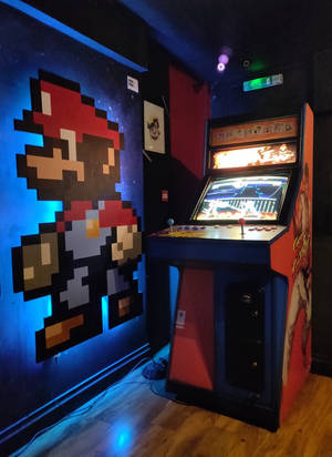 在黑暗的房間中，發光的街機遊戲機旁邊的像素化 Mario 壁畫。 — 街機 壁紙
