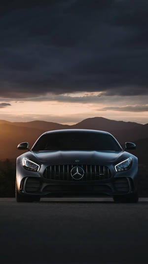 黑色 Mercedes-AMG GT 跑車在暮色中停在路上，背後有山脈。