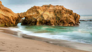 海灘上的天然岩石拱門，碧綠色海浪湧入。 — 7680x4320 壁紙