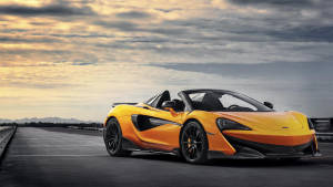 日落時分賽道上的橙色McLaren跑車與戲劇性的雲層。 — 麥拿侖 GIF 壁紙