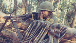 士兵在樹林中瞄準重型機槍，彈藥帶纏繞在圓木上。