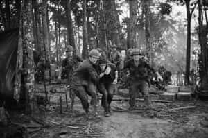 士兵抬著一名受傷的戰友穿過泥濘的叢林營地。