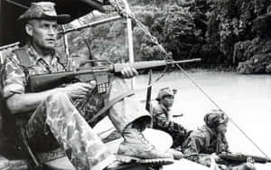 三名身穿迷彩軍服的武裝士兵在叢林環境中的河船上。