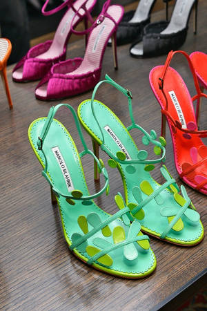 色彩繽紛的 Manolo Blahnik 高跟鞋，帶有花卉鏤空設計，在木質展示架上。