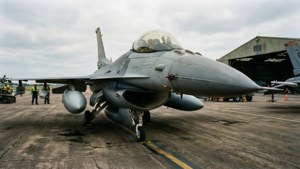 灰色戰鬥機在機場停機坪上，背景有地勤人員和機庫。