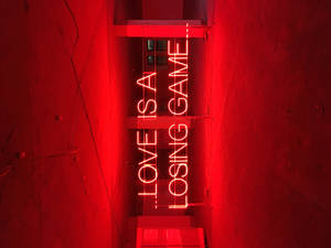 混凝土小巷中寫著「LOVE IS A LOSING GAME」的紅色霓虹燈牌。