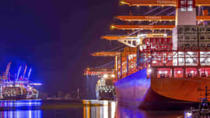 夜間景觀，一艘貨船停泊在港口，有發光的起重機和水面倒影。