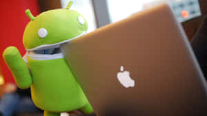 綠色Android毛絨玩具喺銀色Apple手提電腦旁邊。