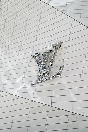 鉻色Louis Vuitton標誌在帶有幾何陰影的白色瓷磚牆上。