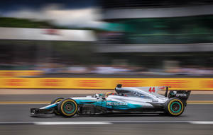 銀色和藍綠色的 Formula 1 賽車在模糊的背景中於賽道上高速行駛。