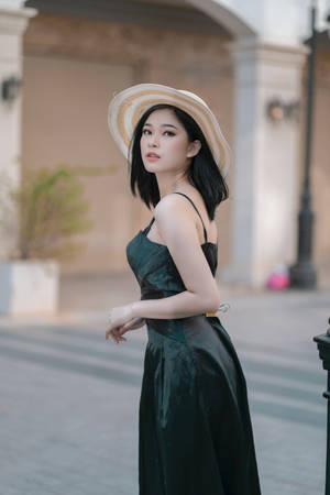 身穿綠色連衣裙和草帽的女性在陽光普照的城市街道上擺姿勢。