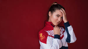 身穿團隊外套的女奧運運動員在紅色背景下將手放在頭上擺姿勢。