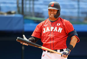 日本棒球選手身穿紅色球衣，緊握球棒，表情猙獰。