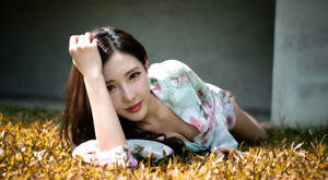 一位穿著花卉連衣裙的女性躺在金色草地上看著相機。