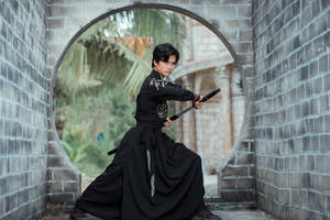 年輕武術家身穿黑色傳統服裝，在石拱門下持劍。