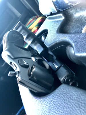 一把黑色左輪手槍放在汽車方向盤上，後面有一塊色彩繽紛的布。 — 槍 壁紙