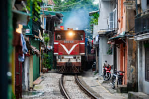 紅色火車在狹窄的城市小巷中行駛，旁邊有電單車和色彩繽紛的建築物。