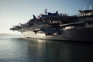 一艘大型航空母艦，甲板上停有飛機，在日落時分停泊在平靜的水面上。