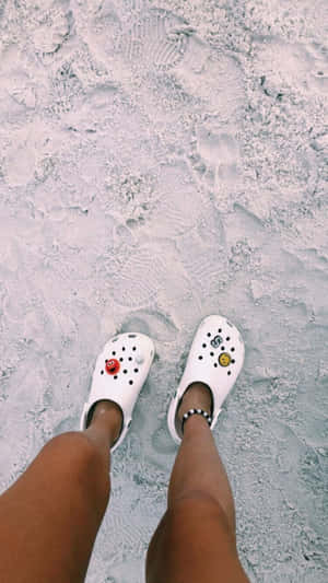 穿著帶有吊飾的白色Crocs鞋的人站在沙灘上。
