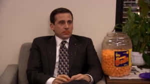 Michael Scott 坐在辦公椅上，旁邊有一個巨大的 Utz Cheese Balls 罐子。