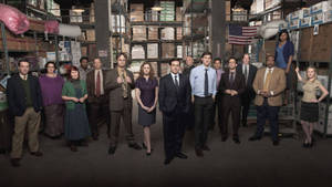 《The Office》演員站在一個有貨架盒子和美國國旗的倉庫中。