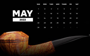 一個帶黑色煙嘴的木煙斗放在黑色背景的2022年5月日曆前。
