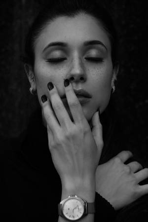 一位閉上眼睛、深色指甲的女人在黑白中輕輕觸摸臉部。