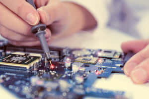 雙手用精密工具將紅線焊接到藍色電路板上。 — MacBook Pro 壁紙