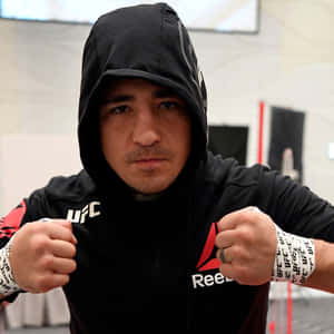 MMA拳手身穿黑色連帽衫和UFC護腕，在健身室中握拳擺姿勢。