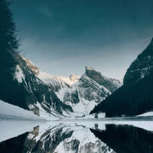 黃昏時分，積雪的山峰倒映在冰凍的湖面上。