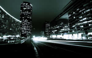夜晚的城市街道，燈火通明的摩天大樓之間有移動車輛留下的光軌。