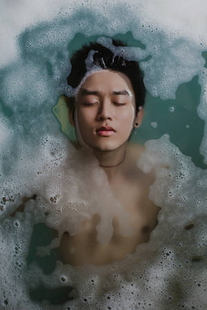 一個閉上眼睛的男子漂浮在藍綠色水的泡泡浴中。