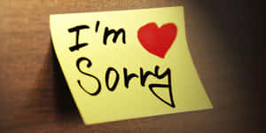 一張黃色便利貼，上面有「I'm Sorry」和一個紅色心形，放在木頭上。