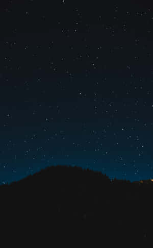 星空夜空下的黑暗森林剪影與遠處的燈光。 — 暮光 壁紙