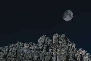 滿月在夜間從尖銳的岩石山峰上升起。