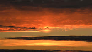 戲劇性的夕陽，帶有熾熱的橙色和紅色雲彩，太陽在黑暗的雲層後方落下。