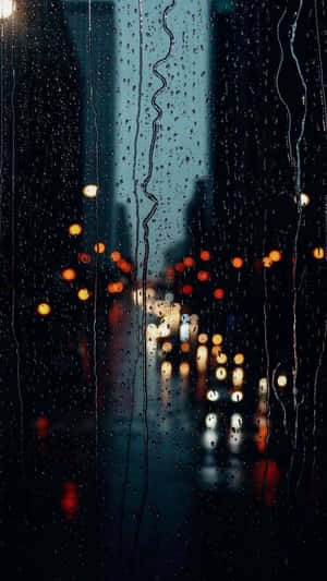雨滴沿玻璃窗流下，顯示夜間模糊的城市燈光。 — 雨 壁紙