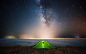 在星空下，銀河在雲海之上，一頂發光的綠色帳篷。