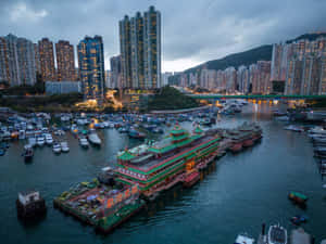 黃昏時分的香港海港，發光的摩天大樓和傳統渡輪停泊在水中。 — 天際線 壁紙