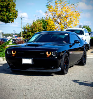 黑色Dodge Challenger SRT，帶有橙色光環頭燈，停在秋樹附近的街道上。