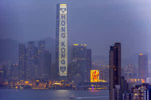 黃昏時分的香港天際線，燈火通明的摩天大樓和港口水面。 — 夜景城市 壁紙