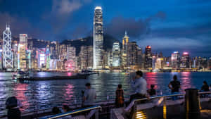 人們在海濱長廊欣賞香港在暮色中燈火輝煌的天際線。 — 天際線 壁紙